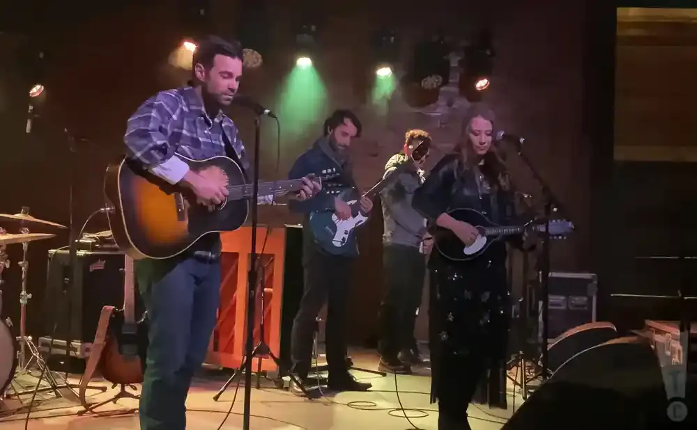 A band performs on stage, with a man singing and playing guitar at the front.