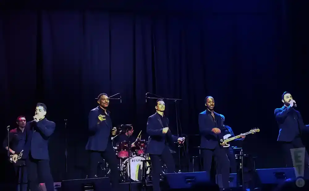 Five men in suits perform on a stage with a dark blue backdrop.