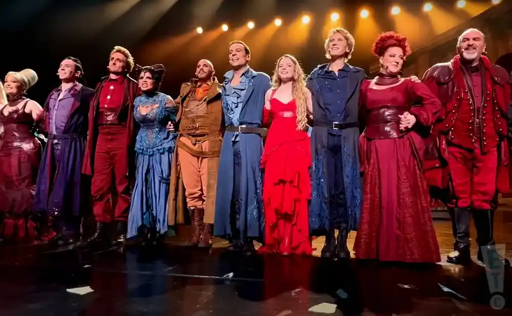 A cast of performers in colorful costumes on stage.