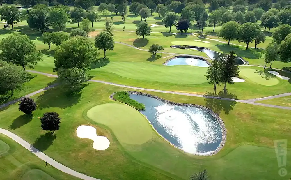 Aerial view of a golf course with manicured greens, sand traps, and water hazards surrounded by trees.