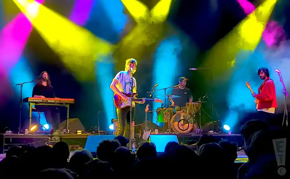 A band performs on a stage with bright yellow and pink lights and fog.