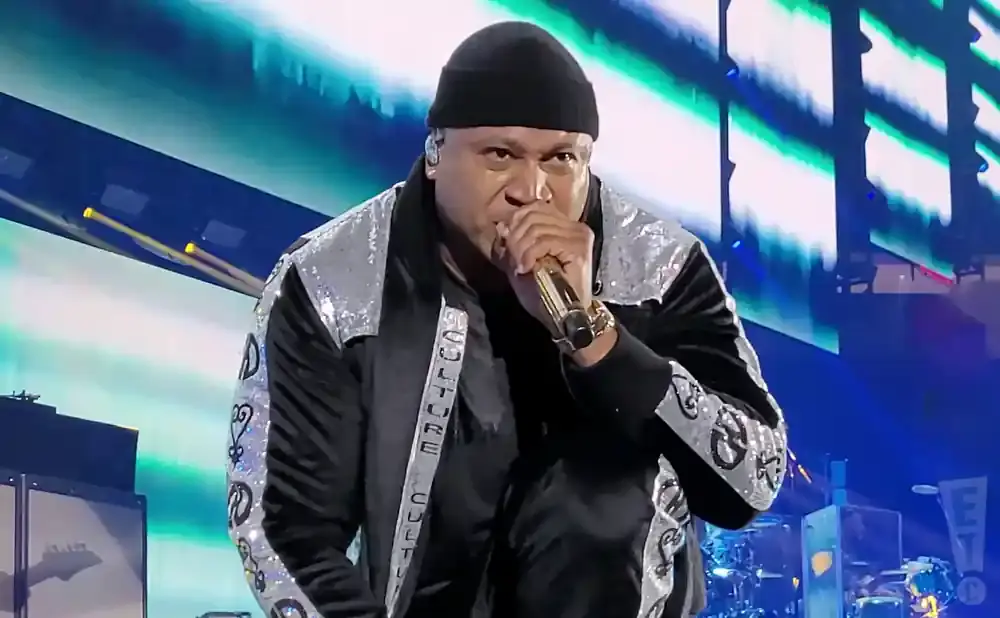 LL Cool J in a black beanie and sparkly jacket performs at a concert.