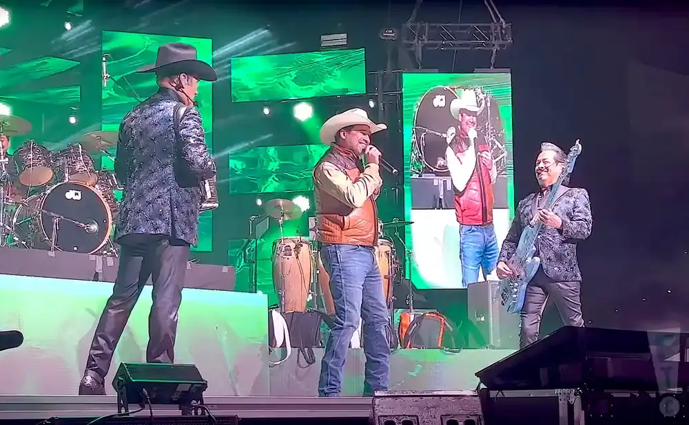 A band performs on stage with bright green screens behind them.