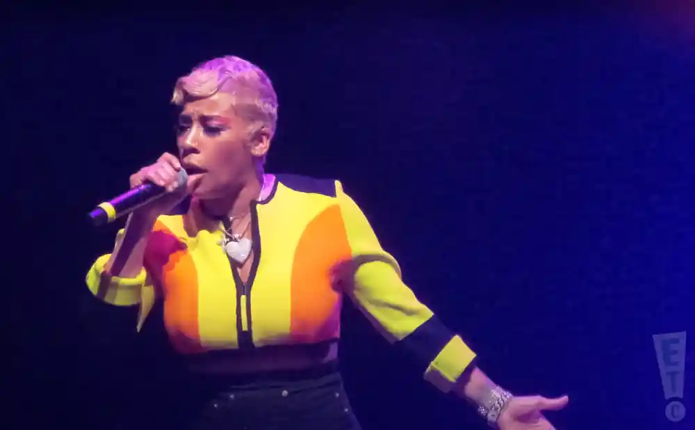Singer with short, blonde hair wearing a colorful jacket and holding a microphone.
