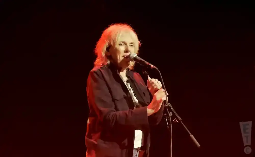 A woman with blonde hair sings into a microphone on a dimly lit stage.