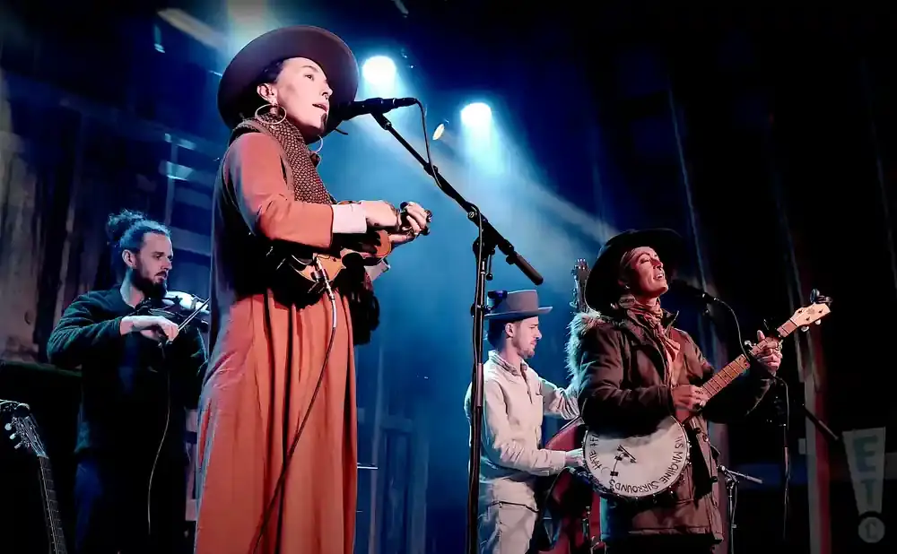 A band performs on stage, with a violinist, ukulele player, and banjo player.