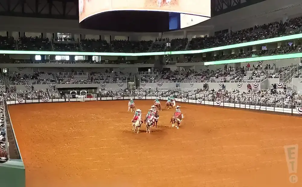 A rodeo event with riders on horses in a dirt arena, surrounded by spectators in stadium seating.
