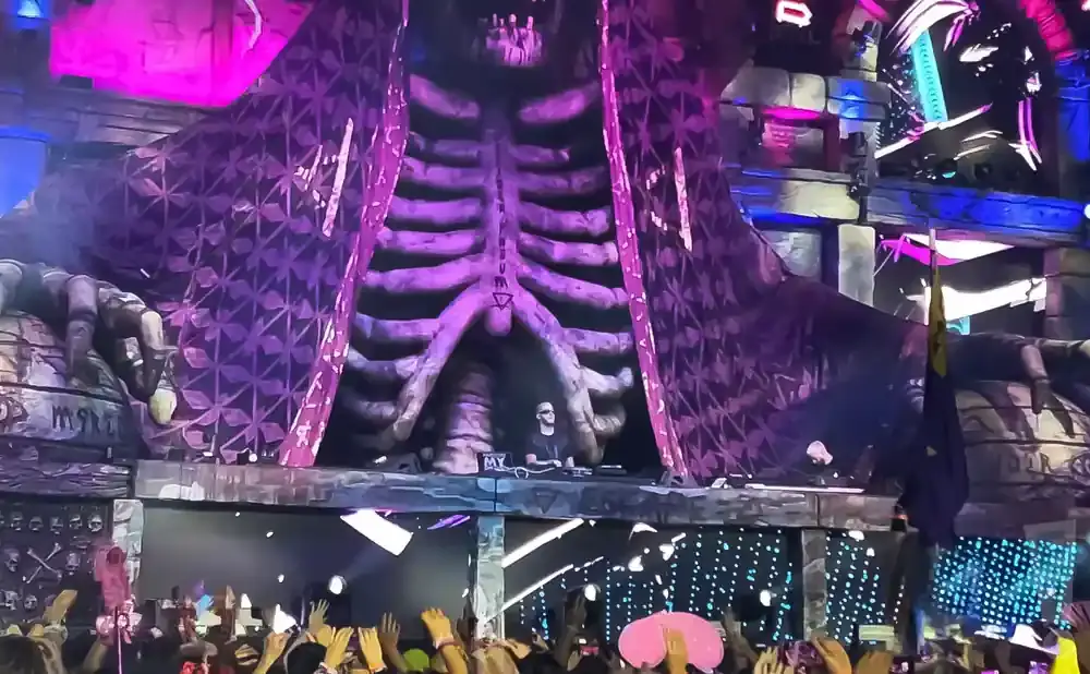 DJ performing on stage inside a giant ribcage structure at a festival.