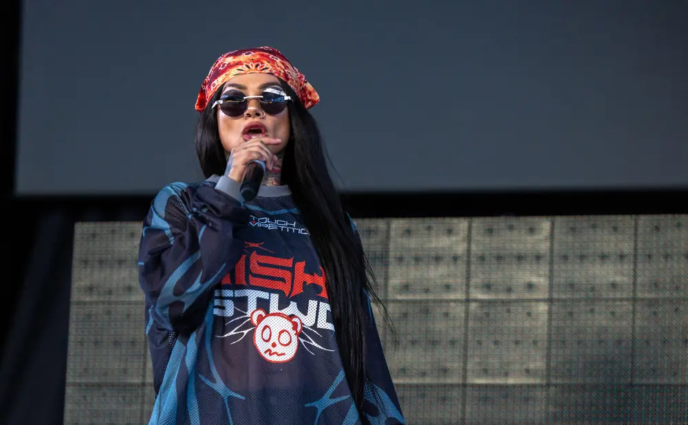 Woman wearing sunglasses and a bandana on stage, singing into a microphone.