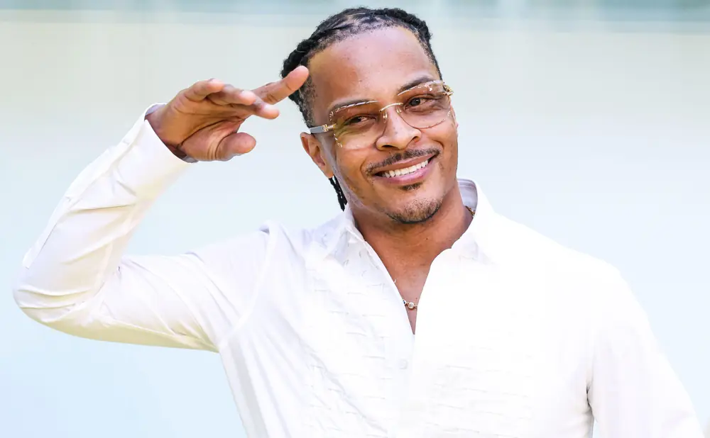Rapper T.I. poses for a photo outdoors, wearing a white shirt and glasses.