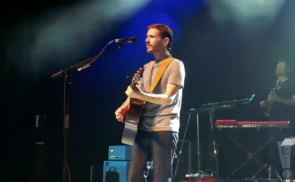 A man plays an acoustic guitar on stage with a microphone in front of him.