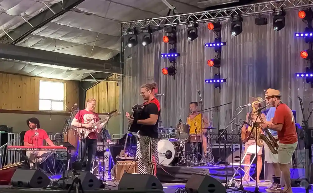A band performs on stage with a guitarist, keyboardist, accordionist, saxophonist, and drummer.