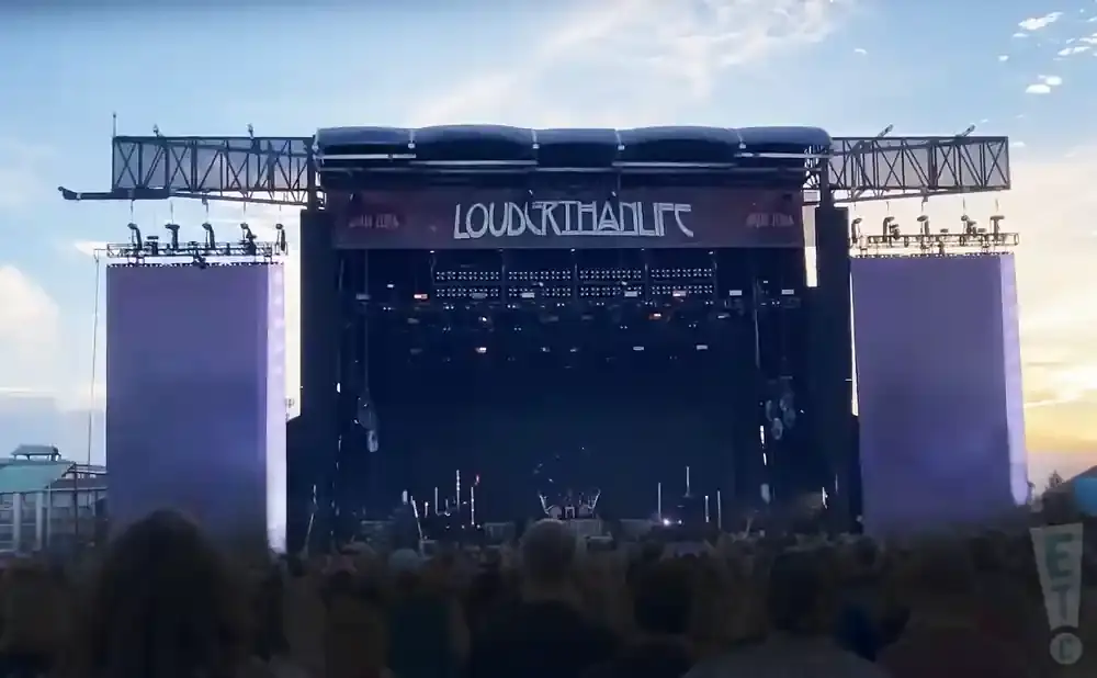 Outdoor concert stage with purple side screens and a crowd of people in the foreground.
