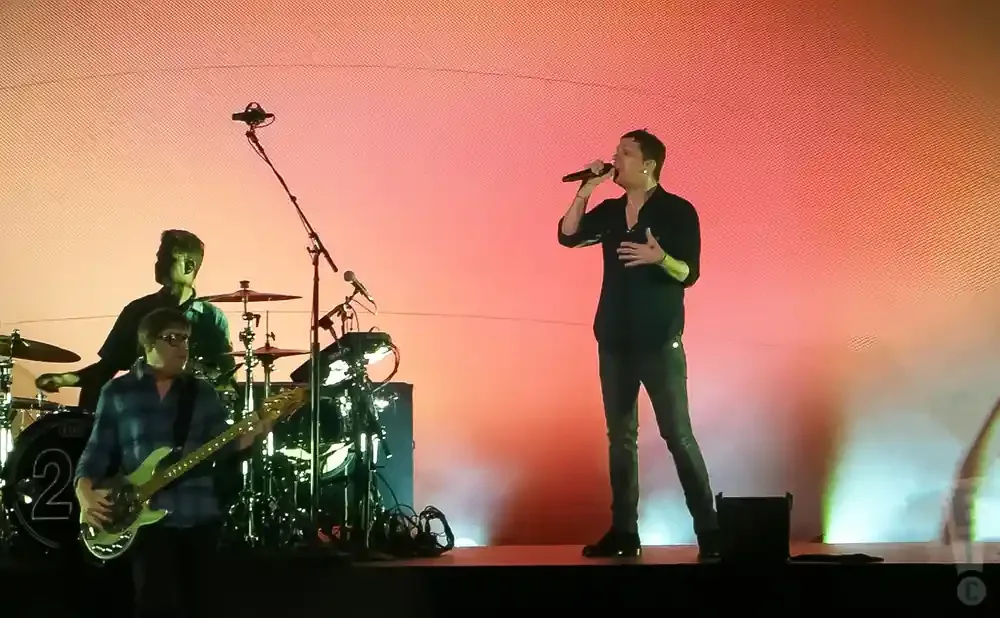 Singer on stage with band, drummer and bassist visible.