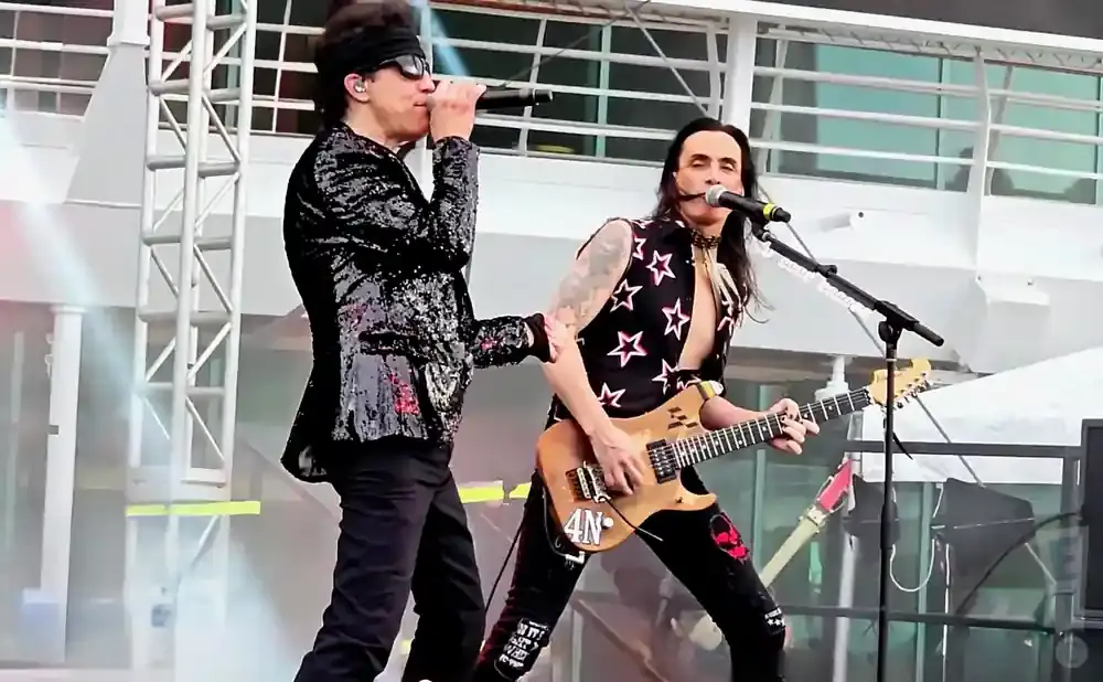 Two male musicians perform on stage; one sings into a microphone, the other plays a guitar.