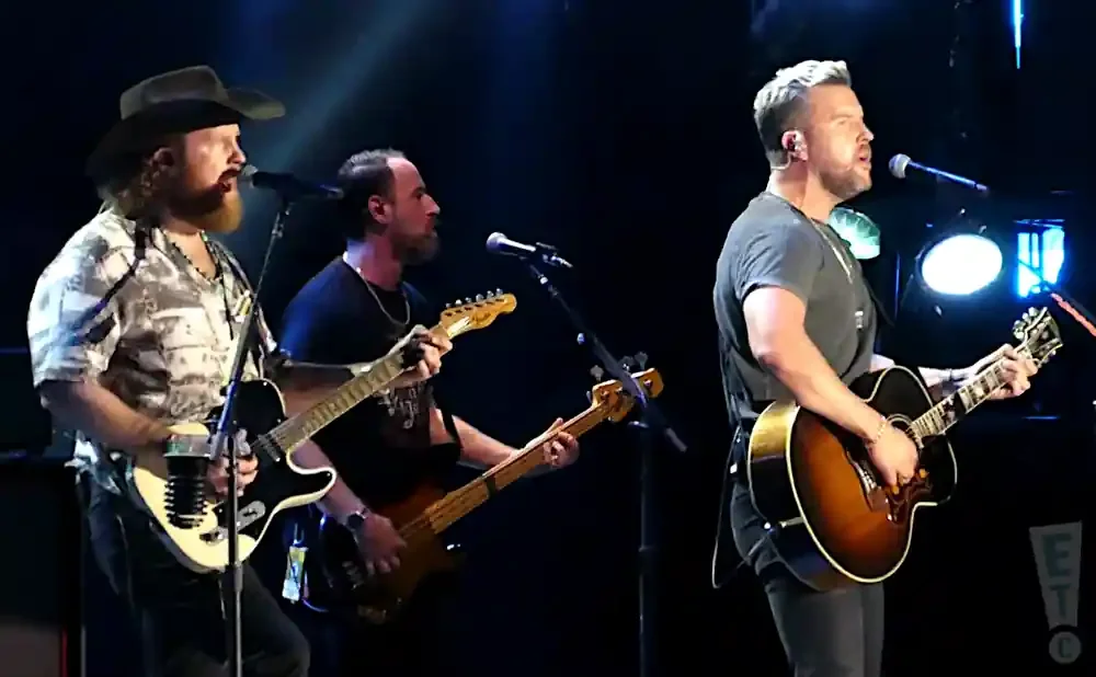 Three male musicians playing guitars on stage.