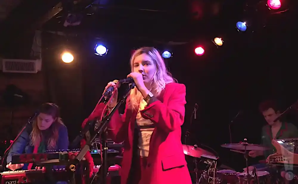 Singer in a red blazer performs with a band on stage under colorful lights.