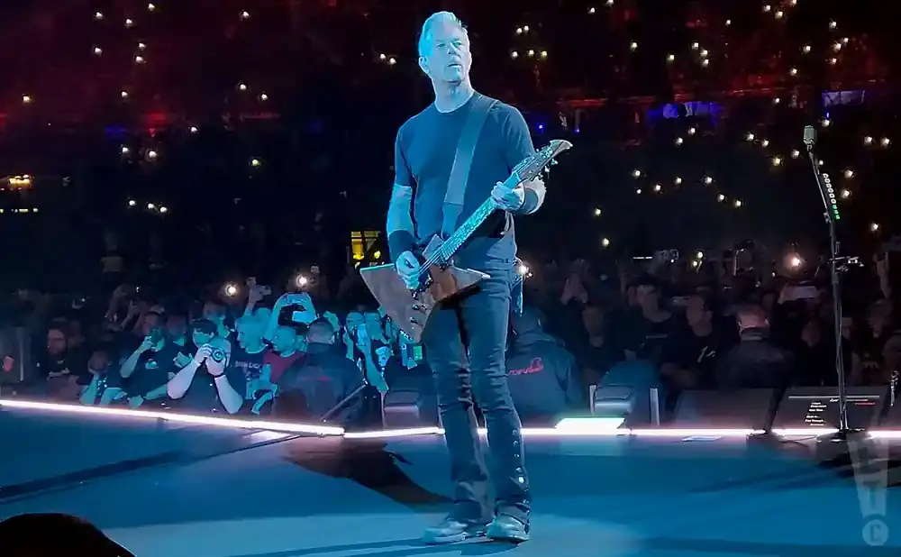 James Hetfield of Metallica performs on stage, playing a guitar in front of a cheering crowd.