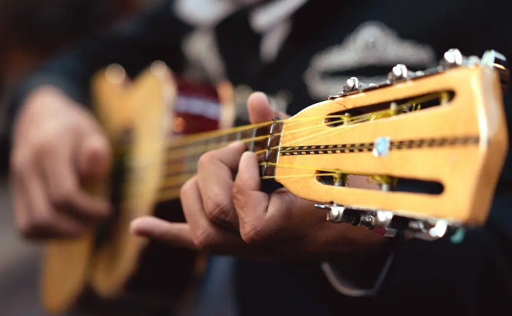 A close-up of a hand playing a guitar, with focus on the strings and fretboard.