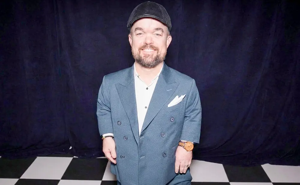 Man wearing a grey suit and cap smiles at the camera.