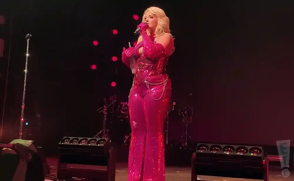 Singer Bebe Rexha performs on stage in a sparkly pink jumpsuit and matching gloves.