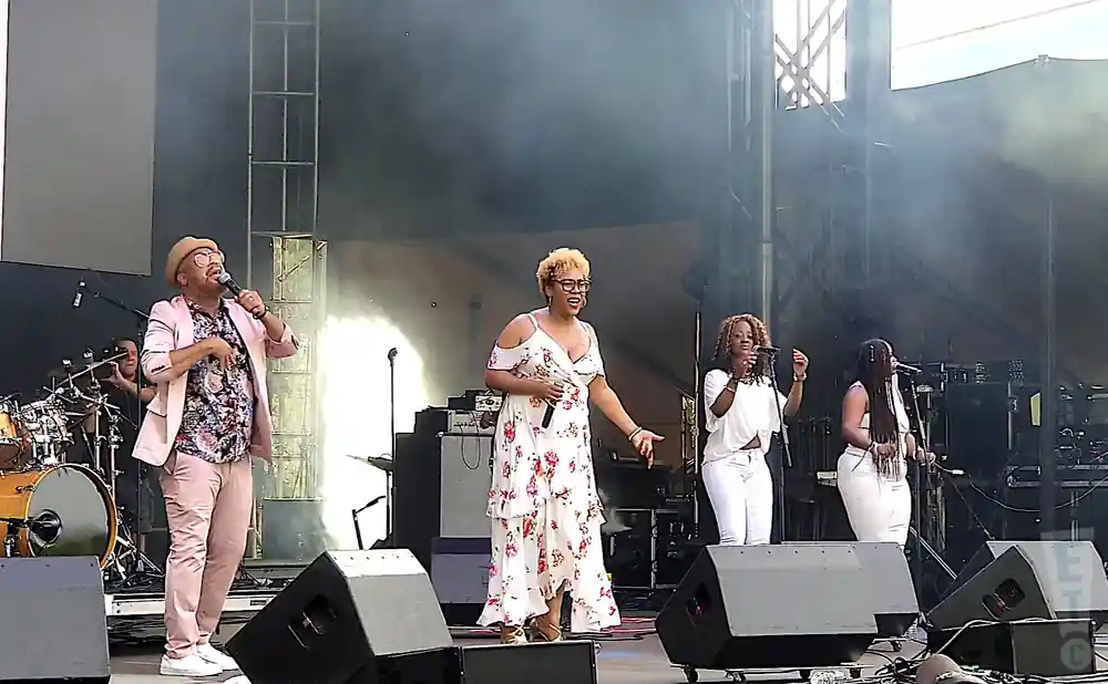 A band performs on stage, with singers in front and drums in the back.