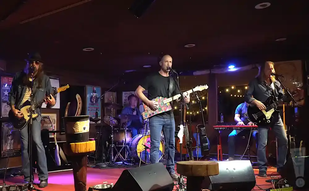 A rock band plays on a stage with a drummer, two guitarists, and a keyboardist.
