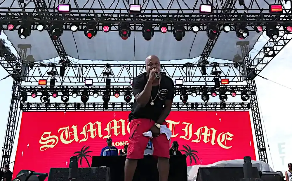 A rapper in red shorts and black shirt performs on a stage with a 
