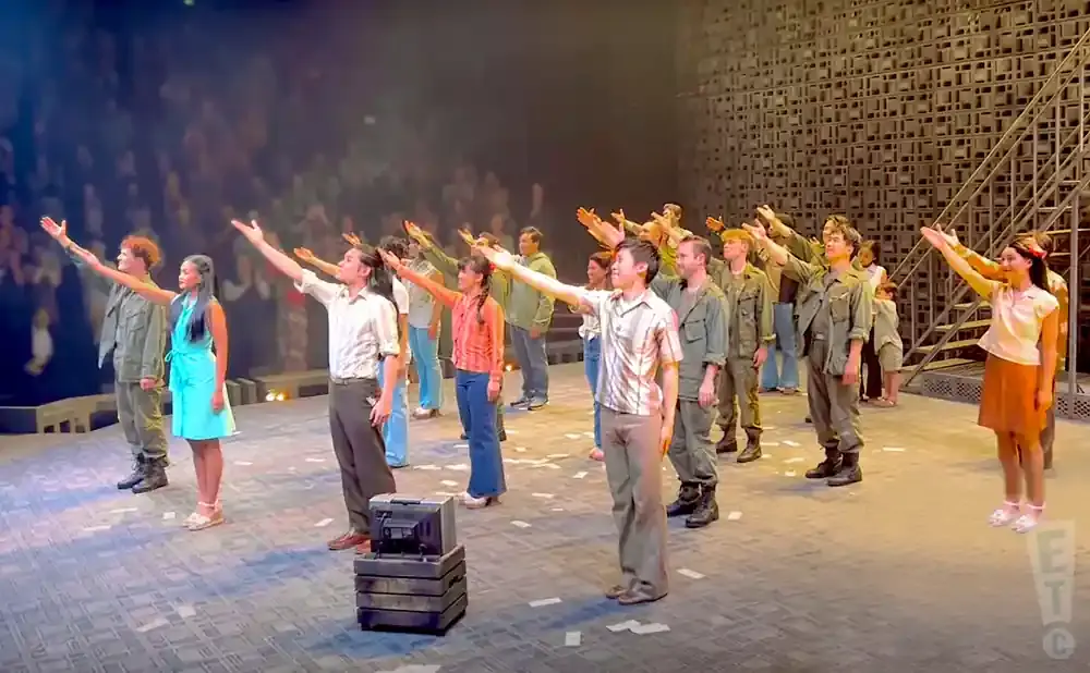 A group of people on a stage with raised arms, some in military-style uniforms.