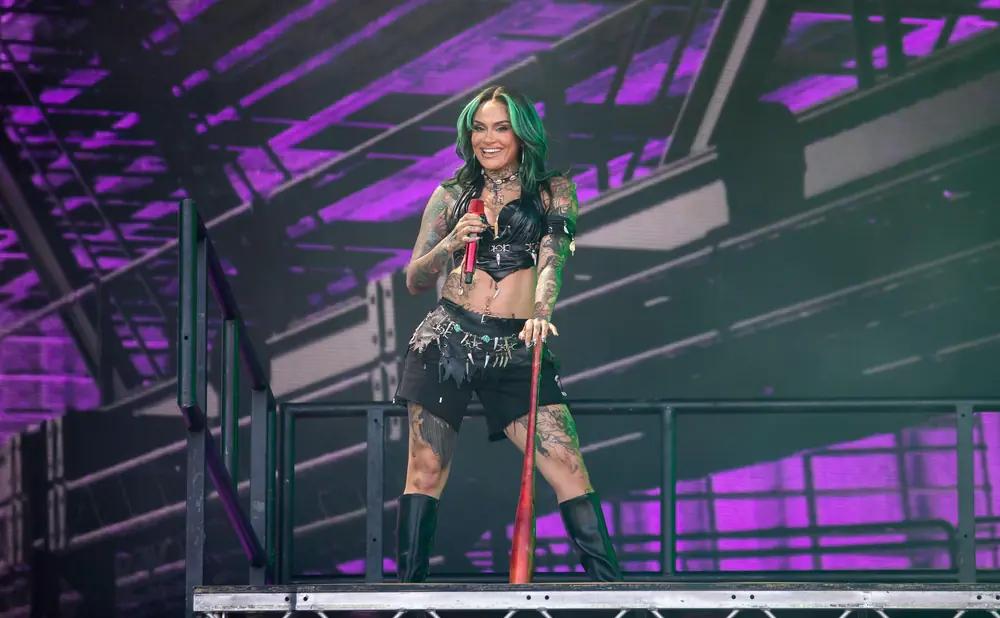 Singer Kehlani performs on stage, holding a red microphone and a baseball bat.
