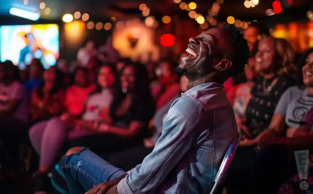 A man laughs heartily at a comedy show while an audience watches in the background.