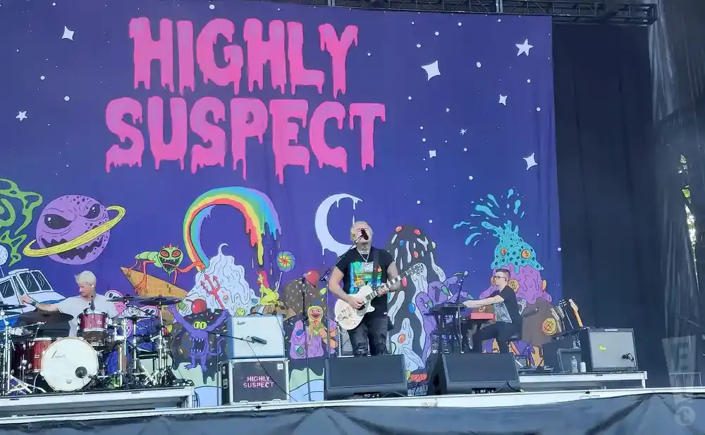 Highly Suspect band performs on stage with a colorful, psychedelic backdrop featuring a starry sky and alien-like creatures.