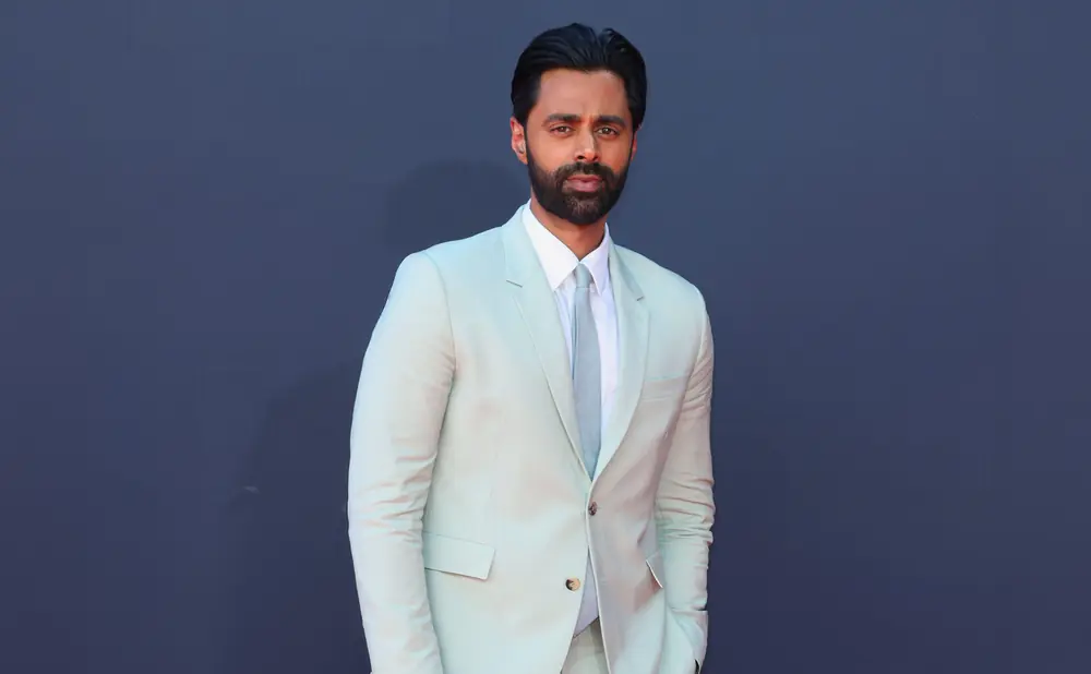 A man in a light mint green suit stands against a dark blue backdrop.