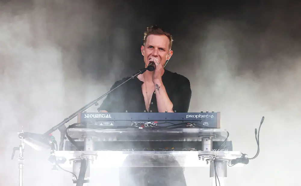 A man plays a synthesizer on stage with smoke effects.