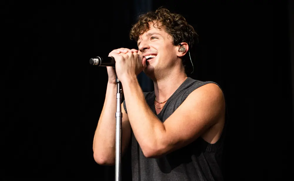 A man with curly hair smiles while singing into a microphone on stage.