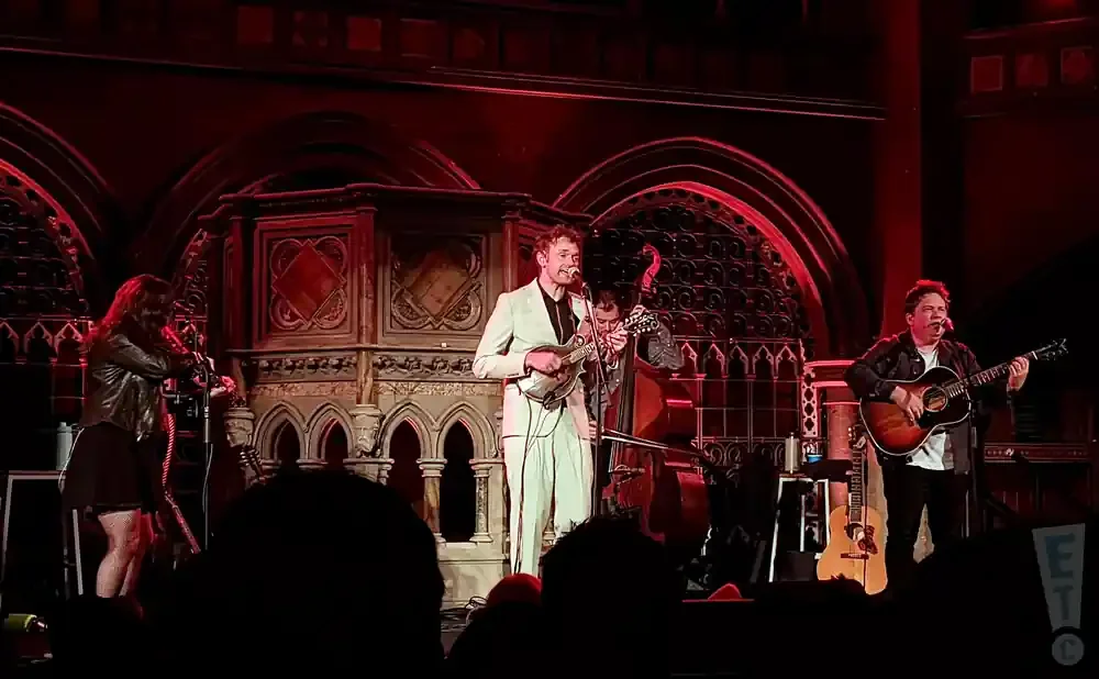 Musicians perform on stage with red lighting and ornate architecture.