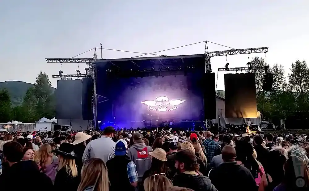 Outdoor concert with a large crowd in front of a stage featuring a skull logo and lighting.