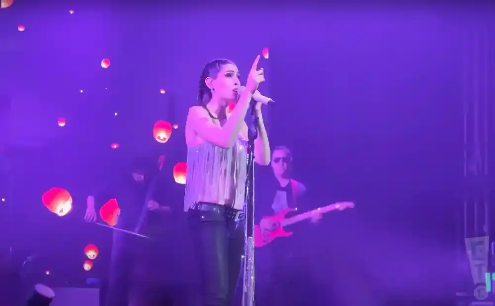 A female singer performs on stage with lanterns floating around her, while a guitarist plays in the background.