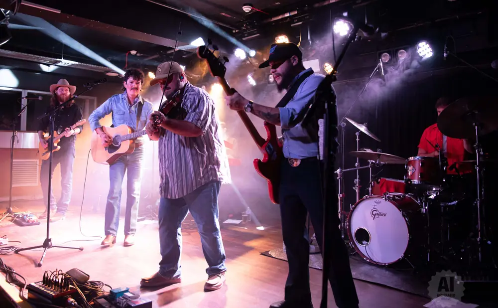 A band plays live music on a stage with colorful stage lighting and smoke.