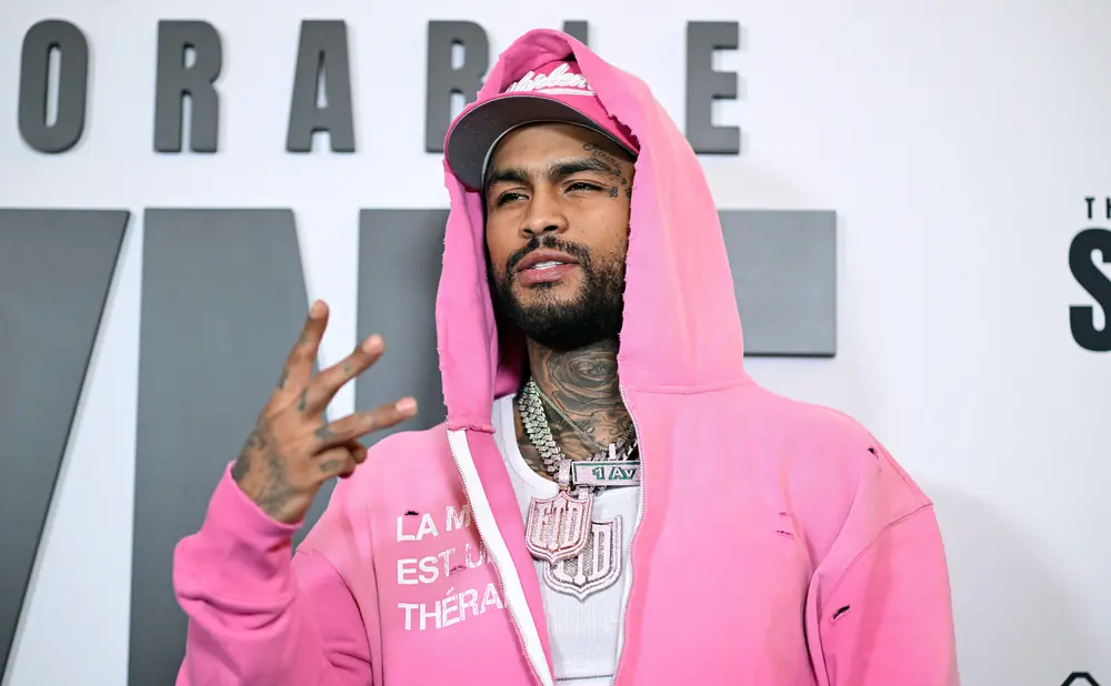 A man in a pink hoodie and cap flashes a peace sign.