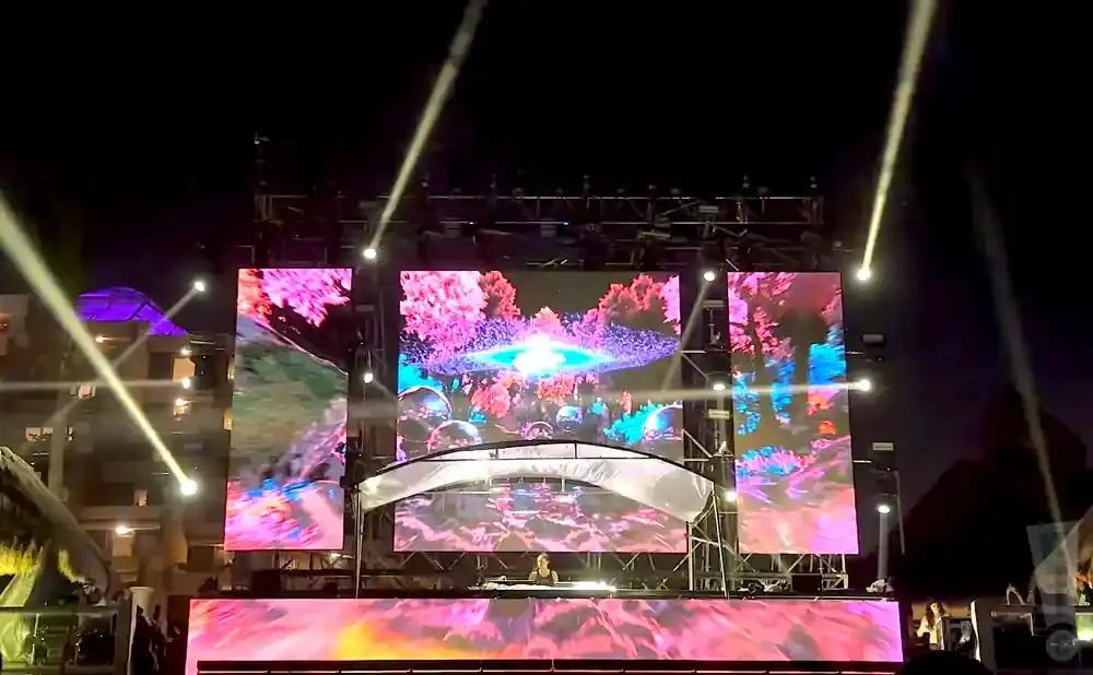 DJ performs on stage with vibrant, colorful screens displaying abstract art and nature scenes.