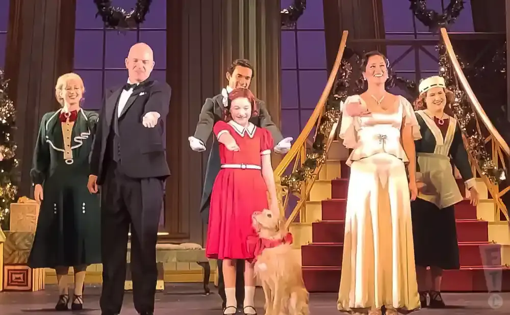 A group of people and a dog on a stage, dressed in festive attire, likely for a holiday performance.