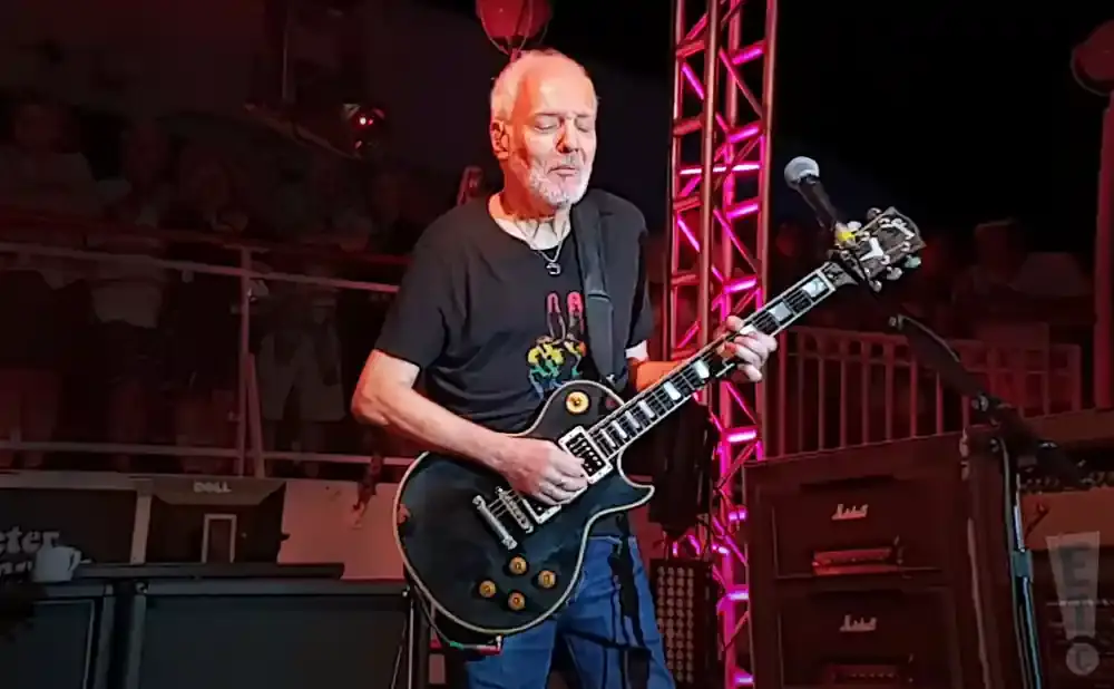 Man playing a black Gibson Les Paul guitar on stage with a microphone and Marshall amps.