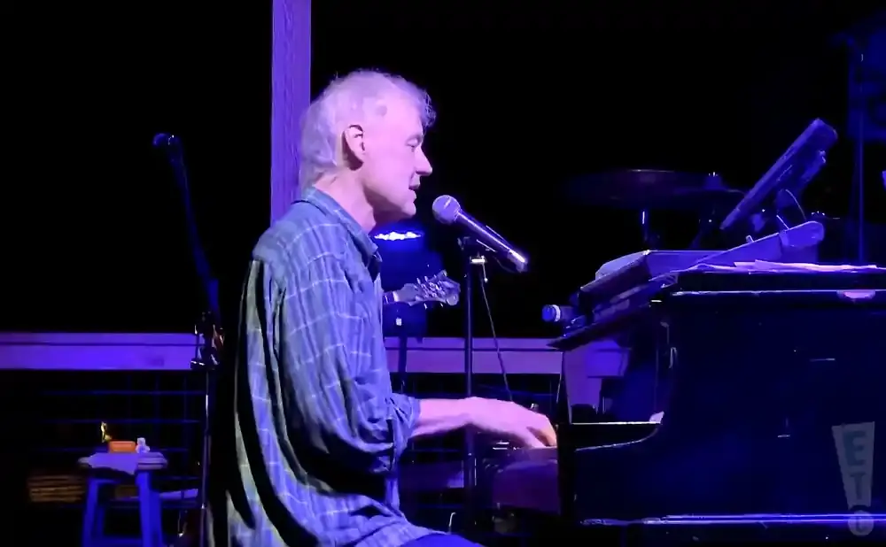 Musician playing piano on stage under purple lighting.