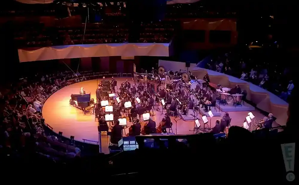 An orchestra performs for a seated audience in a large, circular venue.