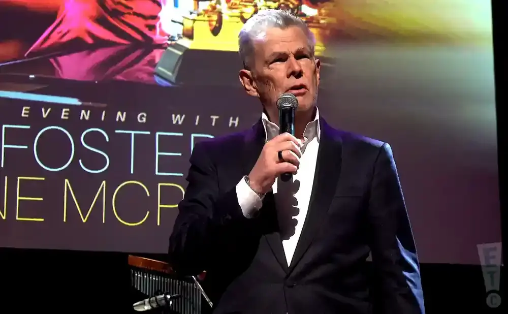 Man in a tuxedo speaks into a microphone on stage, with 