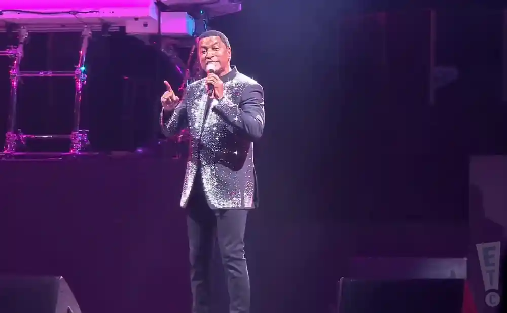 A man in a sparkling jacket sings into a microphone on stage.