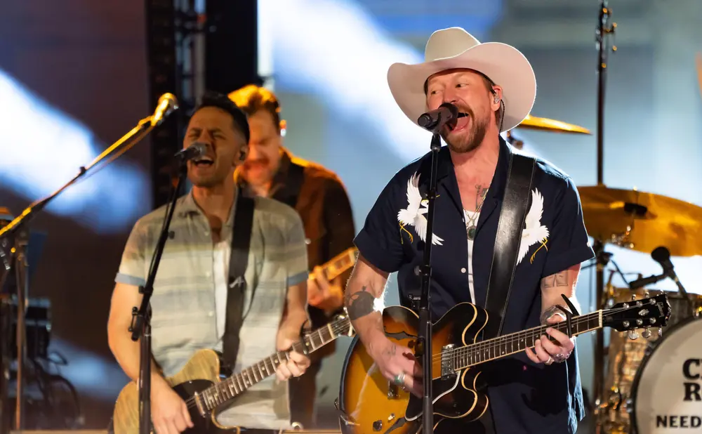 A country singer in a cowboy hat sings and plays guitar on stage with his band.