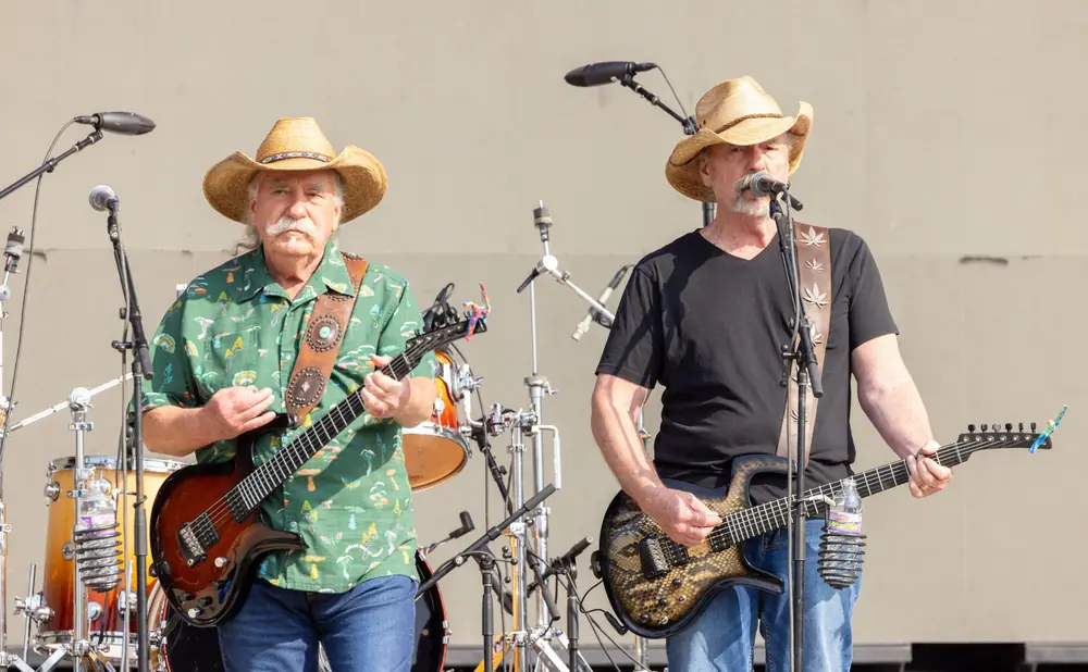 Two men in cowboy hats play guitars on stage, with drums in the background.