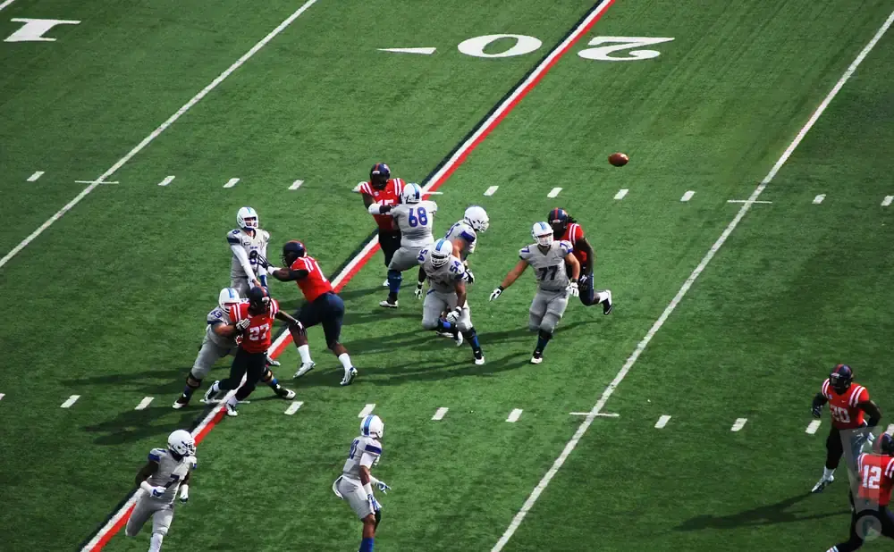 Football players in red and blue uniforms on a green field.